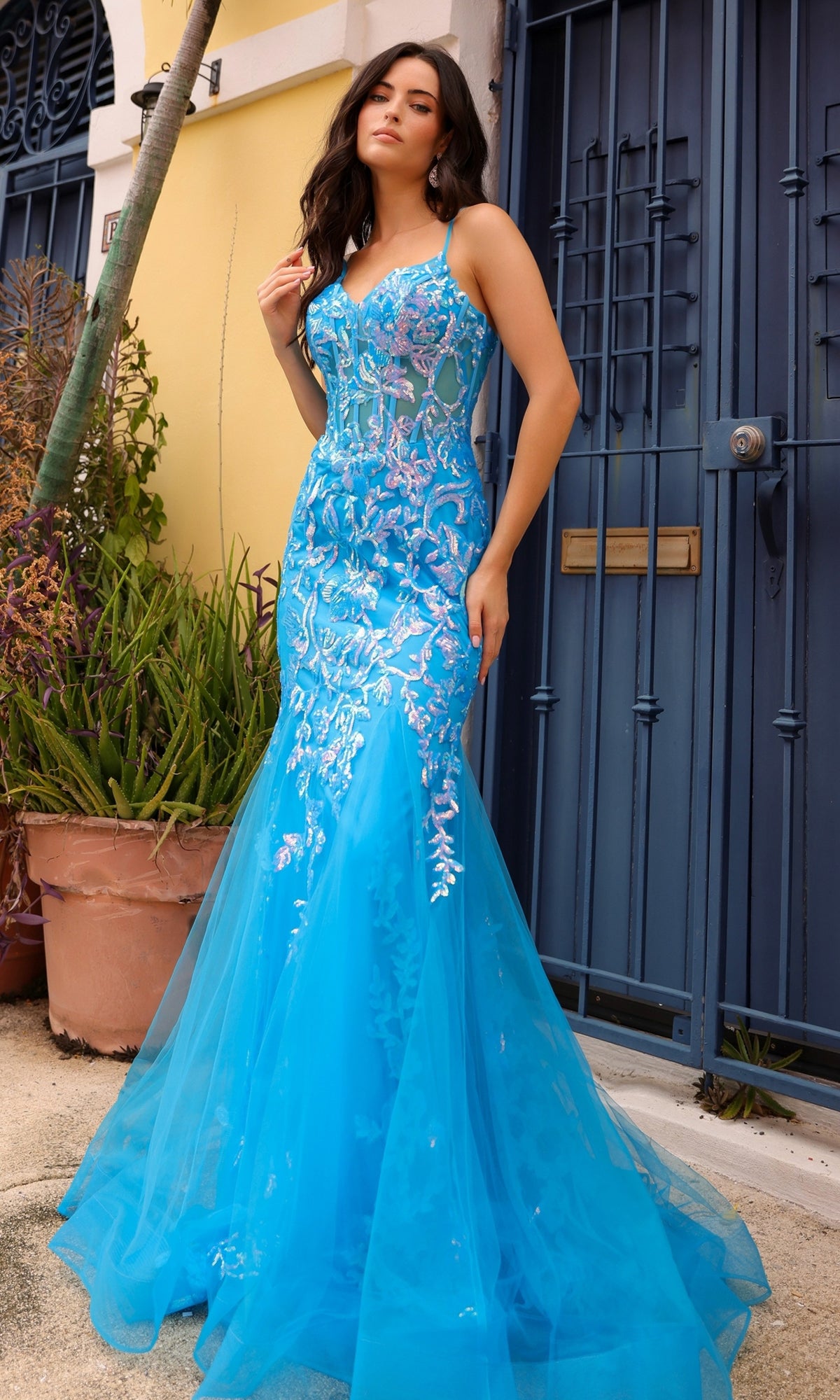 Outdoors, a woman wears the Sequin-Lace Long Neon Mermaid Prom Dress Q1390, featuring floral sequin-lace details, sheer accents, and a bright blue tulle skirt.