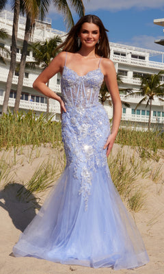 A woman in the Long Embroidered Prom Dress: Nox Anabel Q1541 stands on a sandy beach with grass, palm trees, and a white building in the background.