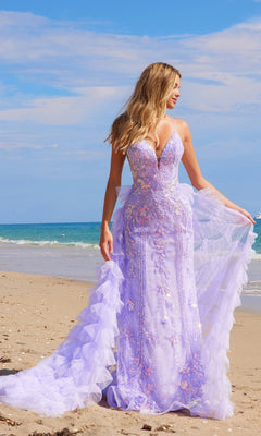 A woman in the Nox Anabel Q1542 ruffled long beaded prom dress stands on a sandy beach, with the ocean and blue sky in the background.