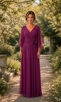 A woman stands on a garden path wearing a Flutter Sleeve Chiffon Long Formal Dress: Rina Di Montella R111 in magenta, featuring a floor-length chiffon skirt, flutter sleeves, and a floral waist accent.