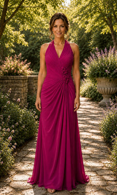 A woman wears a magenta Halter Ruched Chiffon Formal Dress: Rina Di Montella R112, a floor-length evening gown with a ruched bodice and floral waist embellishment, standing on a stone garden path.