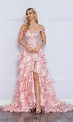 A woman models the Nox Anabel Off-the-Shoulder Lace Prom Dress R1299, featuring a fitted bodice, tiered skirt, and high-low hem, as she stands against a light-colored wall.