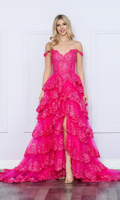 A woman stands against a white paneled wall wearing the Nox Anabel Off-the-Shoulder Lace Prom Dress R1299, featuring bright pink lace, sequin accents, and ruffled high-low detailing.