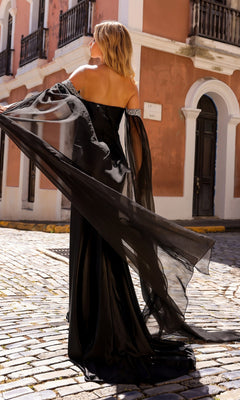 A woman wearing the Off-the-Shoulder Drapes Long Formal Dress R1312 stands on a cobblestone street, framed by peach-colored buildings in the background.