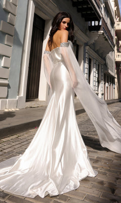 A woman wearing the Off-the-Shoulder Drapes Long Formal Dress R1312 with fitted style and draped sleeves stands on a cobblestone street, facing away from the camera.