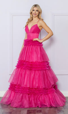 A woman in the Nox Anabel Ruffled Glitter Prom Dress R1316, featuring bright pink tiers and spaghetti straps, stands smiling in front of a light-colored wall.