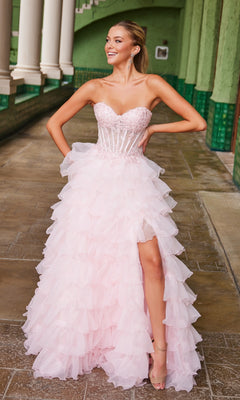 A woman in the Nox Anabel R1688 Strapless Ruffled Prom Ball Gown, light pink with a sheer corset bodice and thigh-high slit, stands on a tiled walkway, smiling and looking to the side.