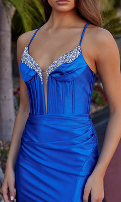 A woman in the Nox Anabel R1689 Lace-Up Long Corset Prom Dress, a fitted royal blue satin gown featuring thin straps, a lace-up open back, and rhinestone accents along the neckline.