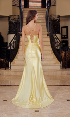 A woman wearing the Nox Anabel R1689 Lace-Up Long Corset Prom Dress in yellow satin stands at the bottom of a grand staircase, her back to the camera, showcasing the open lace-up back.