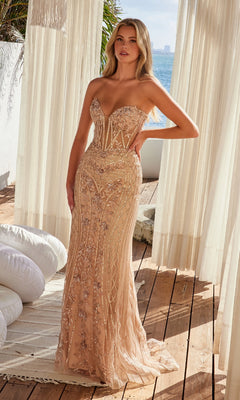 A woman stands on a wooden deck near sheer curtains, wearing the Nox Anabel R1695 Strapless Long Beaded Prom Dress with intricate embroidery and a beaded sheer overlay, with the ocean visible in the background.