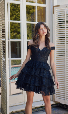 A woman poses by open white shutters in a Nox Anabel R877 Short Ruffled Lace Hoco Dress, with greenery and a pool in the background.