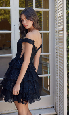 A woman stands before glass doors in the Nox Anabel R877 Short Ruffled Lace Hoco Dress, looking over her shoulder with a neutral expression.