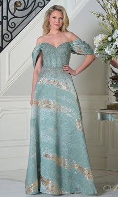 A woman is indoors wearing the Rina Di Montella RD3405 long formal dress in seafoam, featuring a fitted beaded bodice, metallic gold accents, and an elegant A-line organza skirt.