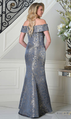 A woman with long blonde hair wears the Rina Di Montella RD3511 long formal dress, featuring a metallic brocade fabric, off-the-shoulder neckline, and mermaid silhouette while standing on stairs in an elegant interior.