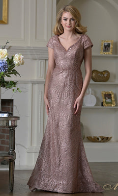 A woman stands indoors in the Rina Di Montella RD3532, a dark mauve floor-length formal dress with lace beading, short sleeves, V-neckline, and mermaid silhouette—ideal for a fashionable mother-of-the-bride.