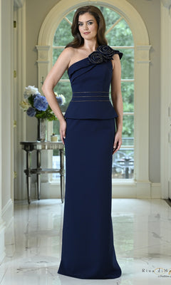 A woman wears a navy One Shoulder Peplum Two-Piece Formal Dress: Rina Di Montella RD3600, featuring a peplum waist, a beaded belt, and a floral accent on the shoulder.