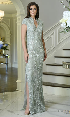 A woman wears a seaglass-colored Cap Sleeve 3D Leaf Fitted Formal Dress: Rina Di Montella RD3602, featuring a cap-sleeve fitted silhouette, V-neckline, and intricate 3D leaf appliques.