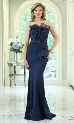 A woman wears a navy Strapless Organza Ruffle Mermaid Formal Dress: Rina Di Montella RD3618, featuring a ruffled bodice and a beaded waist detail.