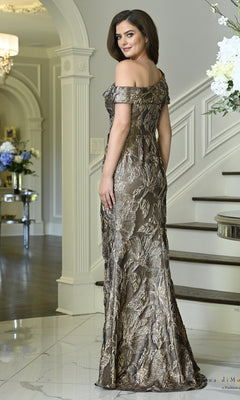 A woman wearing a Metallic Side Bow Long Formal Dress: Rina Di Montella RD3621, a metallic, off-the-shoulder, floor-length evening gown with a floral pattern and a side bow detail.