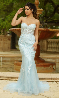 A woman poses outdoors by a stone fountain in the Velvi Long Strapless Lace Mermaid Prom Dress Reva, a light blue gown featuring elegant lace and a mermaid silhouette—perfect for prom.