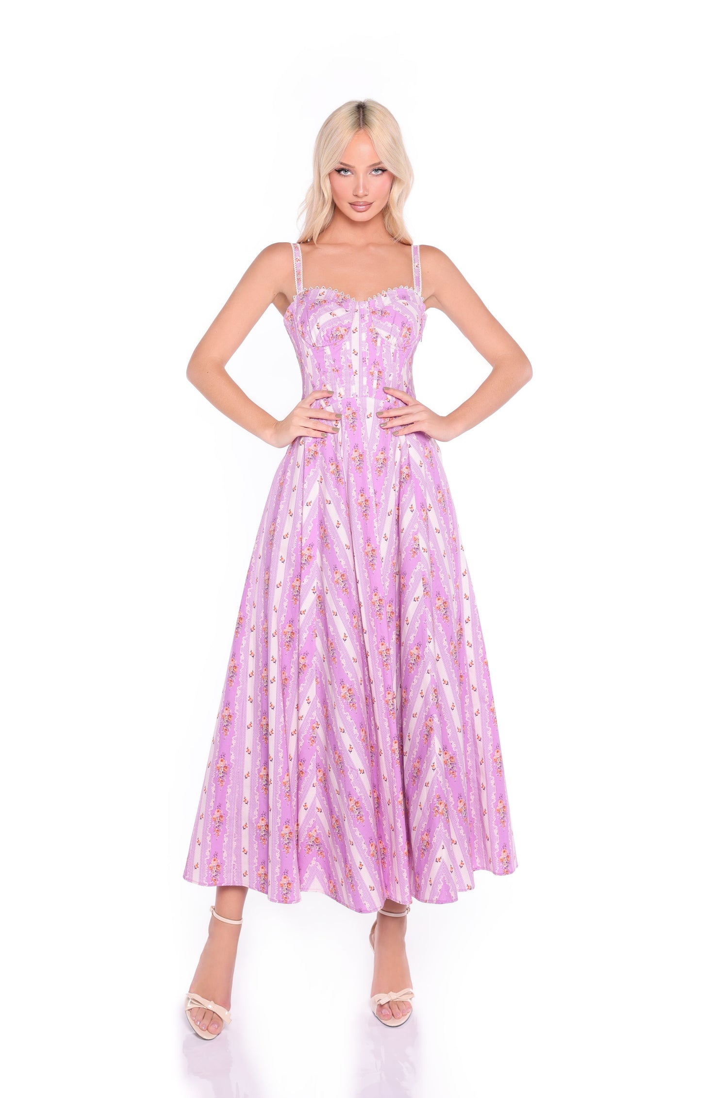 A woman stands against a white background wearing the Rosella Lavender Lilac Floral Casual Midi Dress, which features a floral print, sleeveless design, fitted corset bodice, and flared skirt.