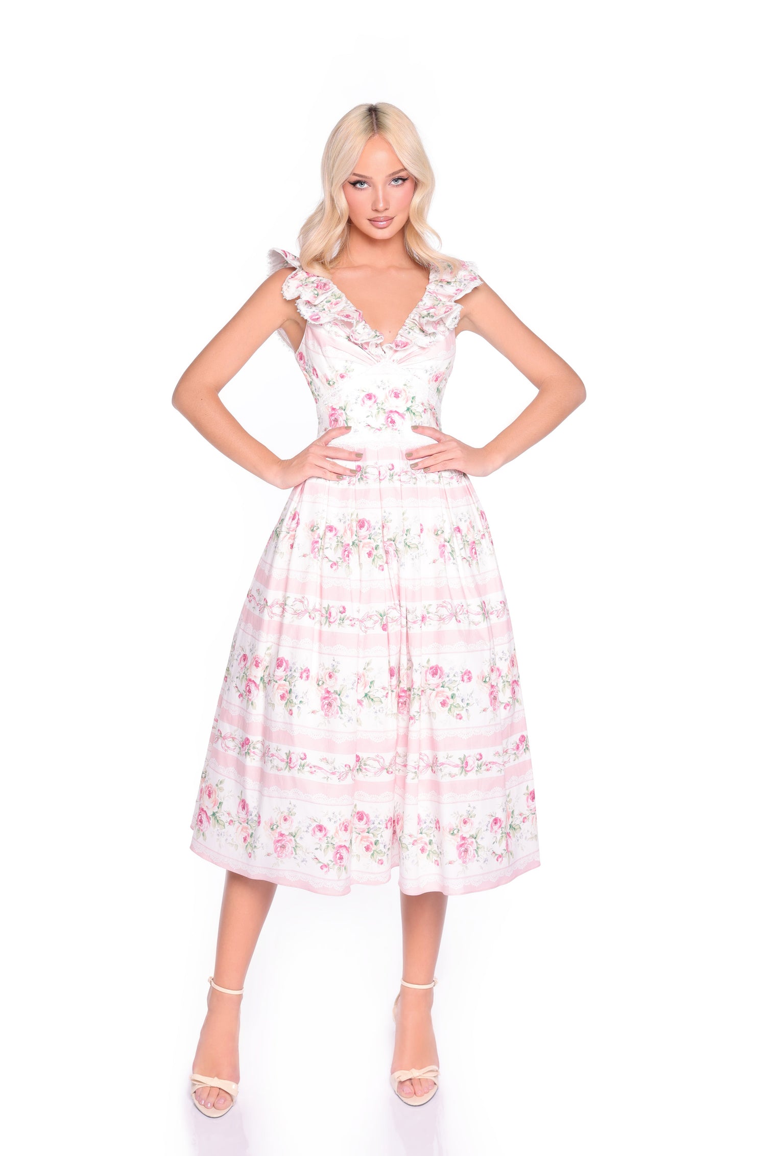 A woman stands with hands on hips against a plain white background, wearing the Pink Floral Casual Midi Dress: Rosette, featuring a sleeveless design with ruffled straps and a delicate floral print.