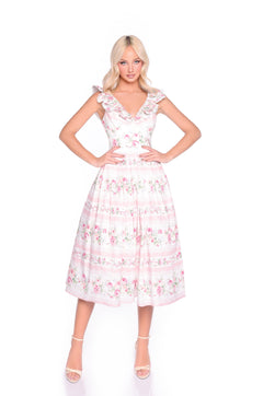 A woman stands with hands on hips against a plain white background, wearing the Pink Floral Casual Midi Dress: Rosette, featuring a sleeveless design with ruffled straps and a delicate floral print.