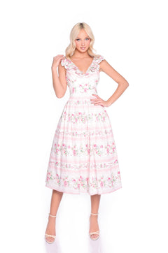 A woman models the Pink Floral Casual Midi Dress: Rosette—a light pink floral midi dress with a ruffled neckline and sleeveless design—styled with white strappy heels against a white background.