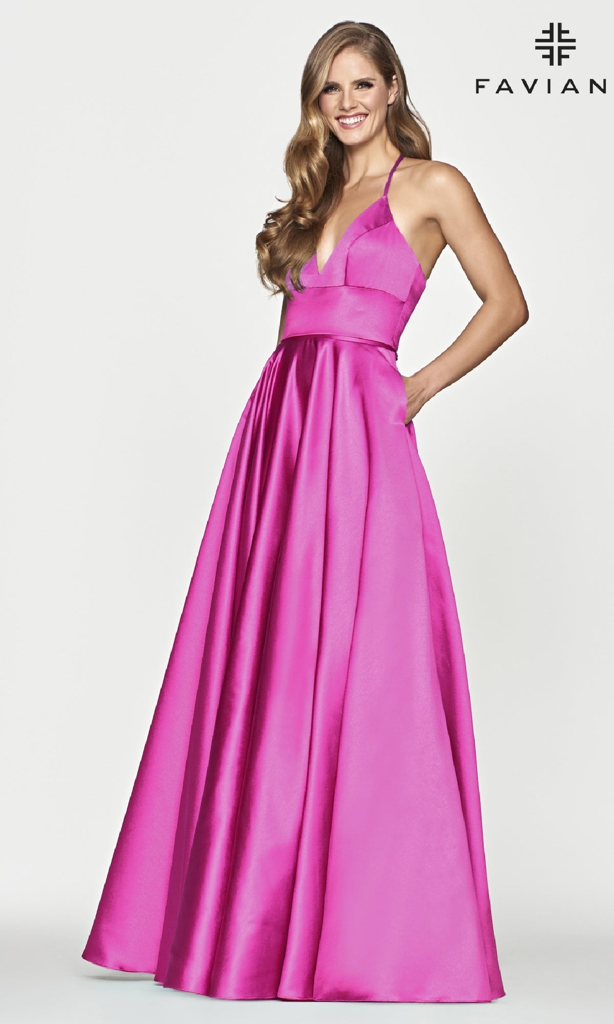 A woman smiles and poses in the Corset-Back A-Line Long Satin Prom Dress by Faviana, a bright pink floor-length satin gown with a deep V neckline, against a plain white background. The 