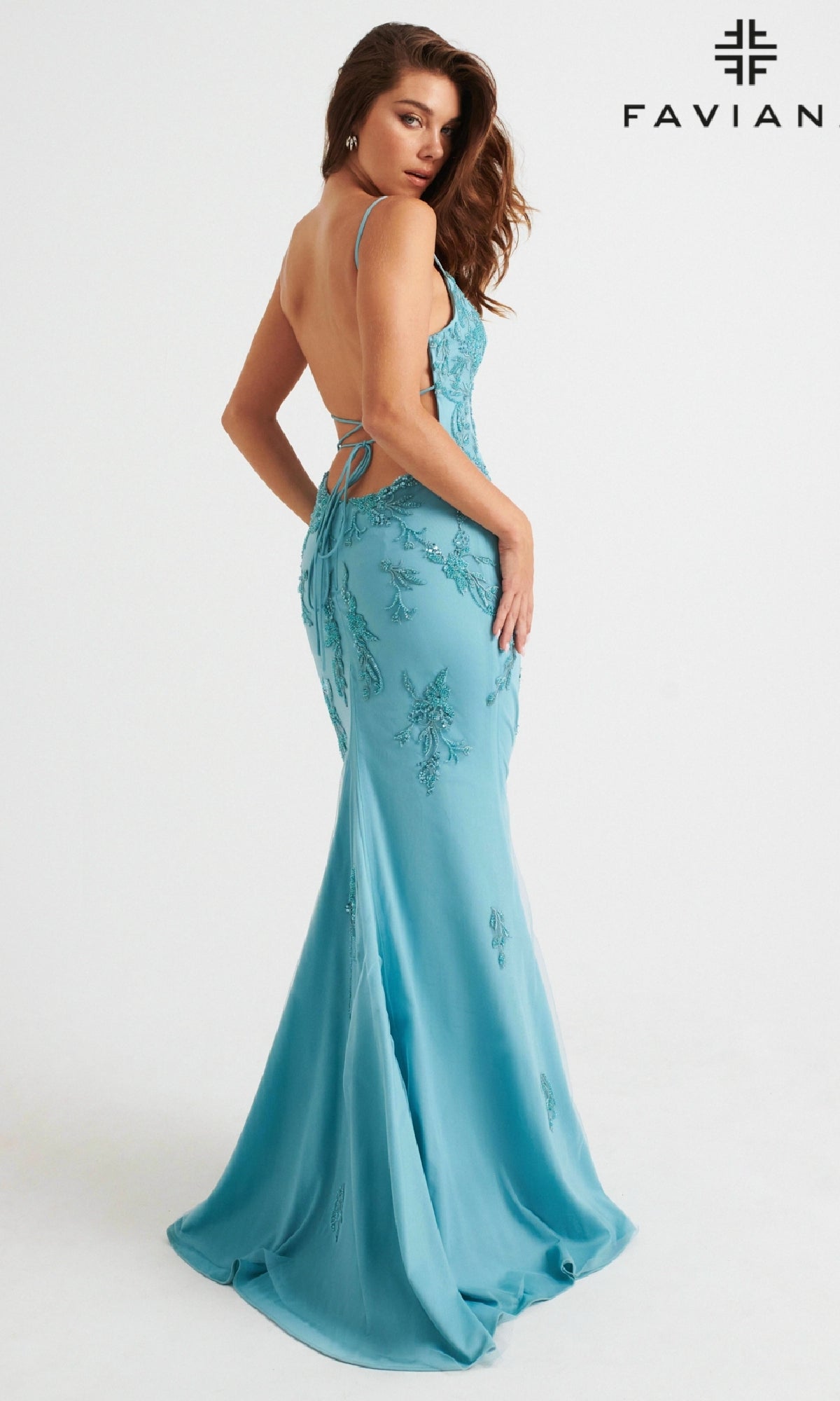 Woman wearing a light pink, floor-length prom dress with a strappy back by Faviana, posing against a plain white background. 