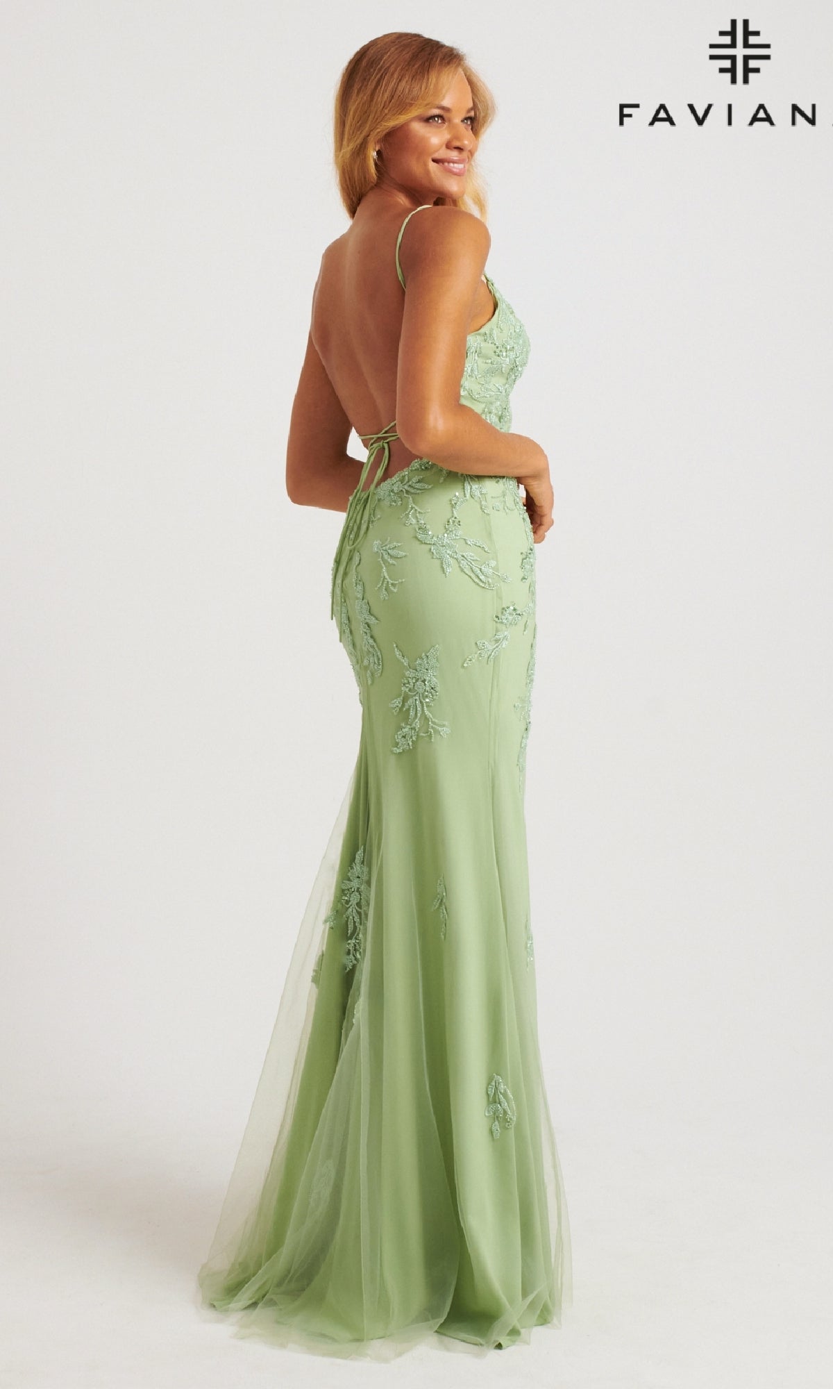 Woman in a strappy-back, long light pink Faviana prom dress, standing and smiling slightly; Faviana logo appears in the top right corner.