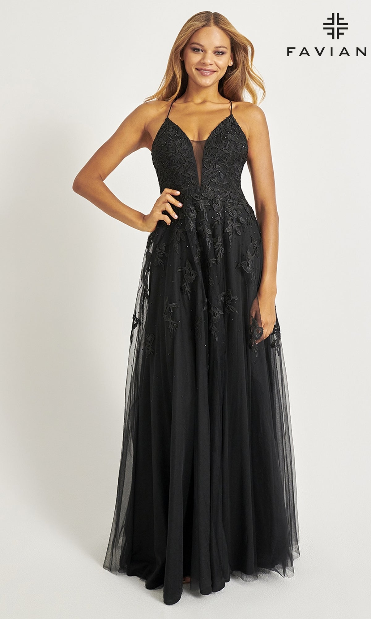 A woman wears the Faviana Embroidered A-Line Long Prom Dress, featuring black lace, thin straps, and 3-D floral embroidery, standing against a plain white background with the Faviana logo in the top right corner.
