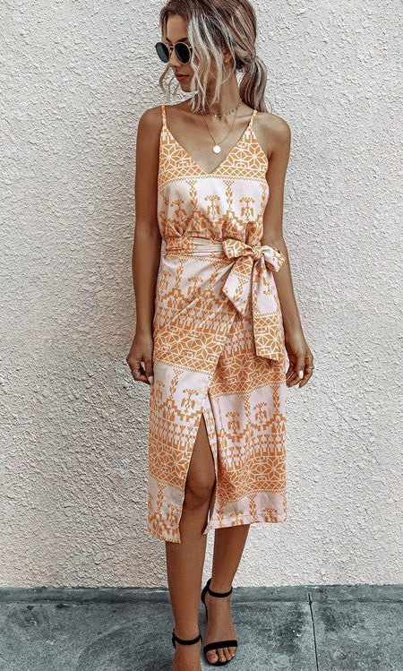 A woman stands against a light textured wall wearing the V-Neck Casual Print Midi Wrap Dress with Front Slit, styled with sunglasses and black sandals.