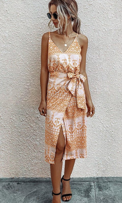 A woman stands against a light textured wall wearing the V-Neck Casual Print Midi Wrap Dress with Front Slit, styled with sunglasses and black sandals.