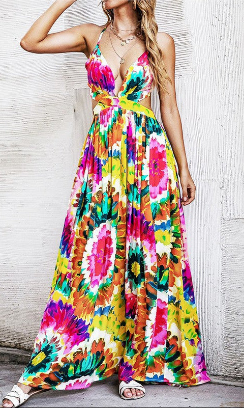 Woman in the Casual Open-Back Colorful Print Maxi Dress with adjustable spaghetti straps and white sandals, standing against a textured white wall.