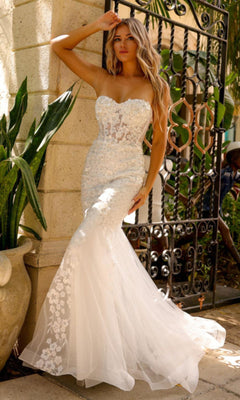A woman in the Amelia Couture Corset Mermaid Prom Dress SU081 poses outdoors by a wrought iron gate and potted plant.