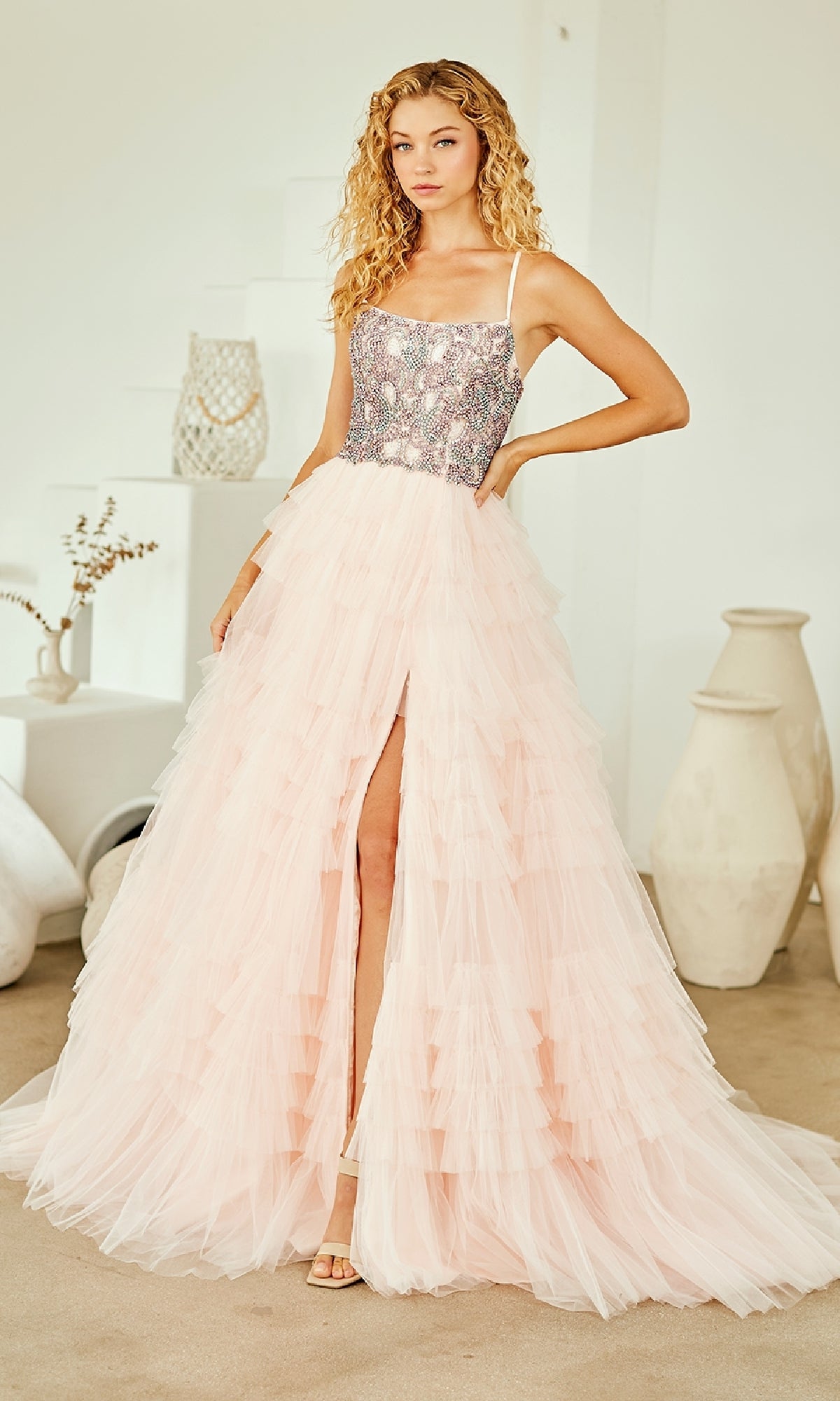 Woman wearing a light pink ball gown with a beaded corset bodice and a full ruffled skirt, standing indoors.
