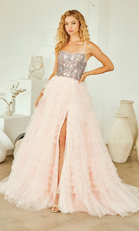 Woman wearing a light pink ball gown with a beaded corset bodice and a full ruffled skirt, standing indoors.