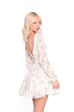 A woman wears the Sadie Yellow Floral Short Casual Dress, featuring a buttercream hue and lace-up back, as she stands looking over her shoulder against a white background.