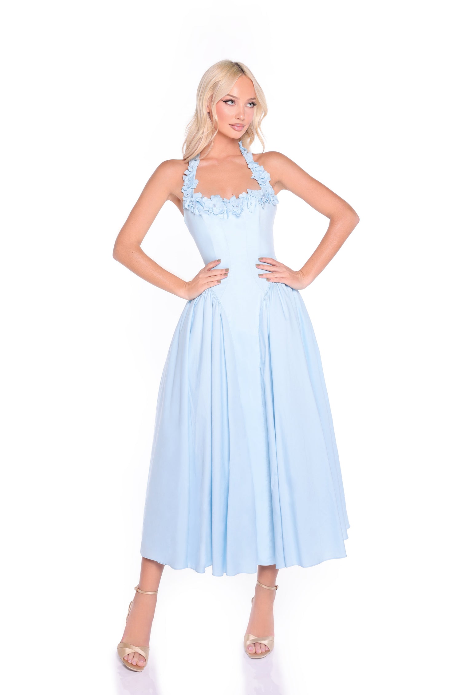 A woman wears the Powder Blue Midi Casual Halter Dress: Skye, featuring a halter neckline and floral detailing, posing with hands on hips against a white background.