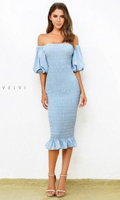 A woman models the Skyla Knee-Length Puff-Sleeve Wedding-Guest Dress in light blue, featuring an off-the-shoulder smocked bodice, puff sleeves, and a ruffled hem, shown against a plain white background.