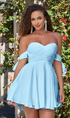 A woman wearing the Velvi Off-the-Shoulder Mini Party Dress Sophie in light blue stands outdoors among greenery and flowers, smiling at the camera.