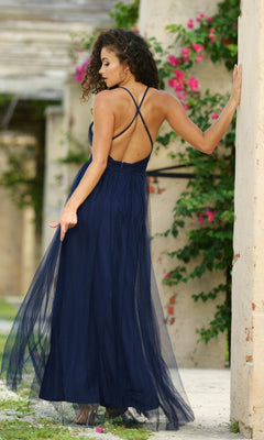 A woman stands outdoors near a concrete pillar, surrounded by pink flowers and greenery, wearing the Velvi Plunging V-Neck Long Tulle Prom Dress Sydney in navy blue.