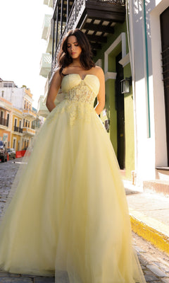 A woman wearing the Strapless Sheer-Waist Long Prom Ball Gown T1326 poses on a cobblestone street with colorful buildings in daylight.