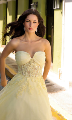 A woman stands outdoors on a sunny day in the Strapless Sheer-Waist Long Prom Ball Gown T1326, the pale yellow dress with lace detailing softly glowing in the sunlight.