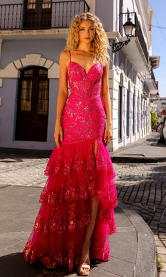 A woman stands on a cobblestone street in front of colonial buildings, wearing the Sequin Long Ruffled Mermaid Prom Dress T1337—a bright pink, sleeveless gown with tiers, sequin accents, and a thigh-high slit.