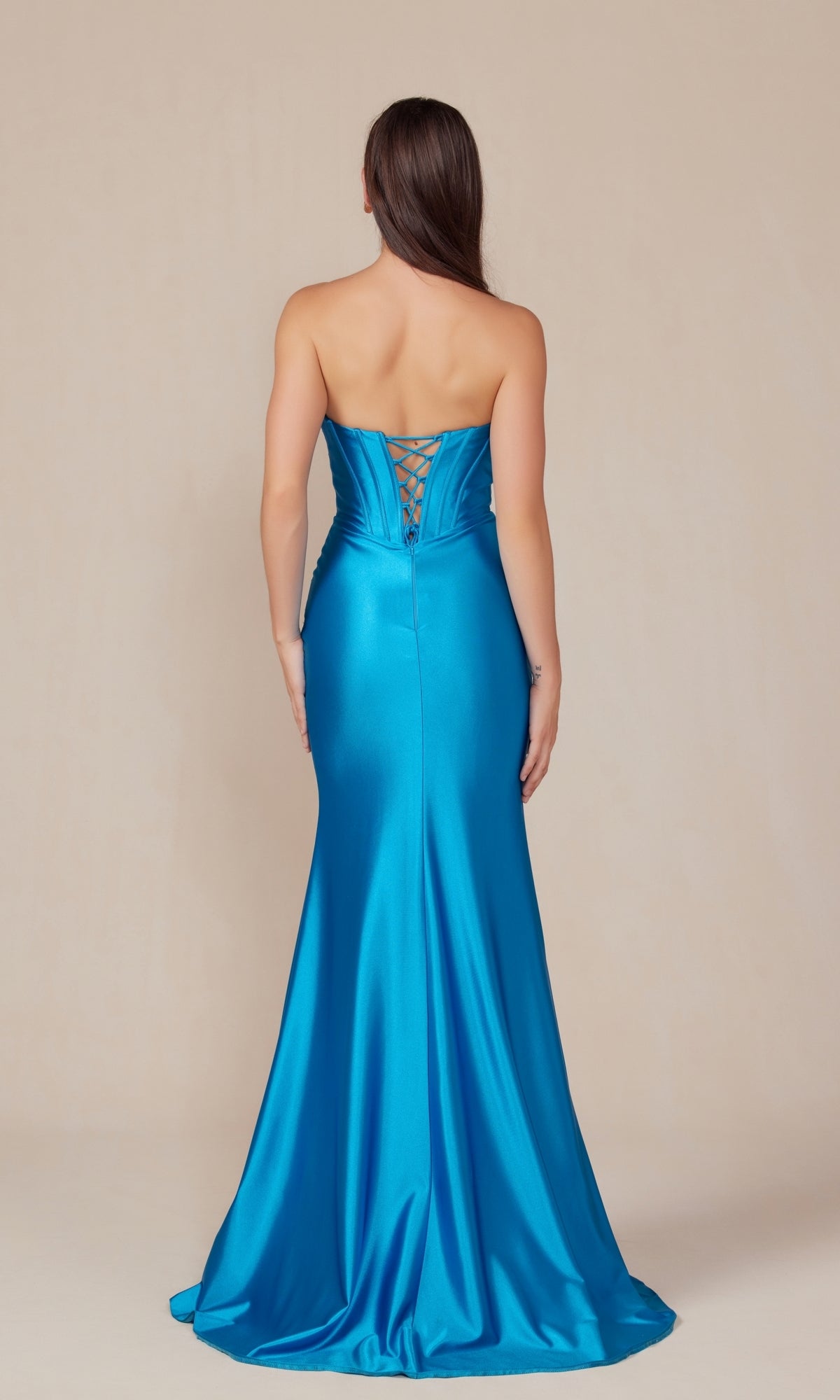 A woman faces away, wearing the Nox Anabel T1500: a strapless long prom dress with a sweetheart neckline, blue satin fabric, corset-style bodice, and lace-up back detail.