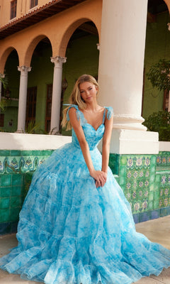 A woman wears the Nox Anabel T1501 Tie-Dye Long Ruffle Prom Dress, posing before a tiled wall with columns and an arched building in the background.