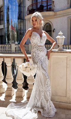 A woman wearing the Tina Holly T19280 Long White Sequin Wedding Gown stands on a balcony, holding a bouquet of white roses with elegant buildings in the background.