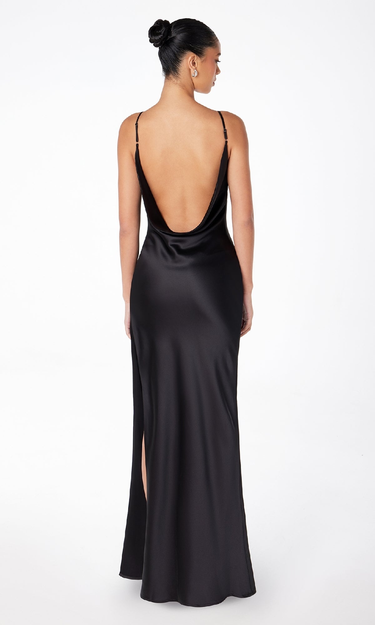 A woman stands with her back to the camera in the Astee T2000 Cowl-Back Sexy Long Prom Dress, a sleek black evening gown with thin straps and a low back, her hair neatly styled in a bun.
